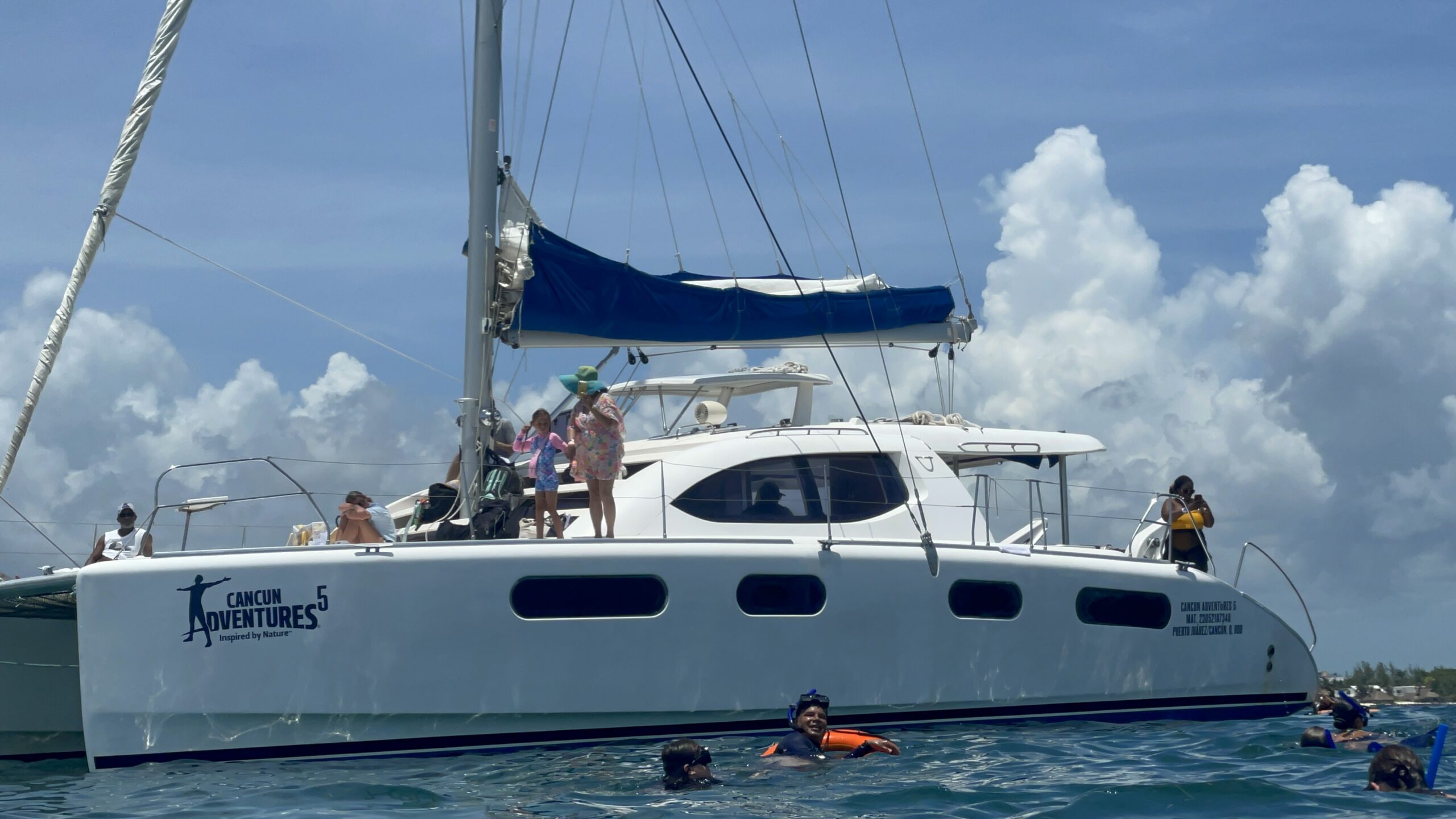 Cancún Adventures catamaran anchored off the coast of Isla Mujeres, with travelers snorkeling nearby in crystal-clear Caribbean water, captured from the waterline perspective.