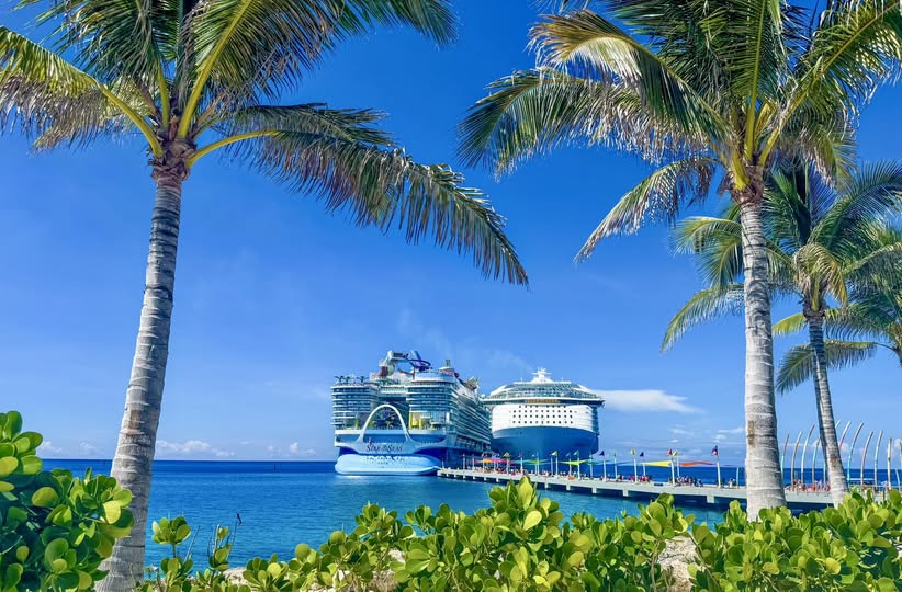 View of two Royal Caribbean Icon ships docked at their private island Perfect Day at CocoCay, from the island shoreline with palm trees and turquoise lagoon which is a must-see stop when you cruise into your dream vacation.